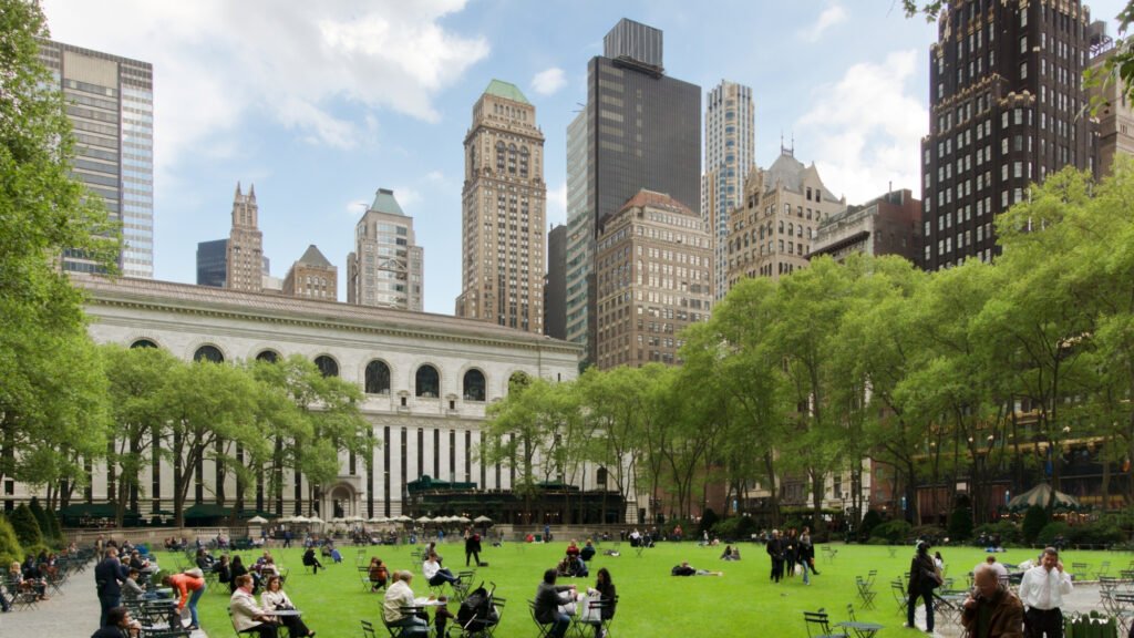 Sprawling green lawn surrounded by flowers and Midtown skyscrapers at Bryant Park next to the New York Public Library.